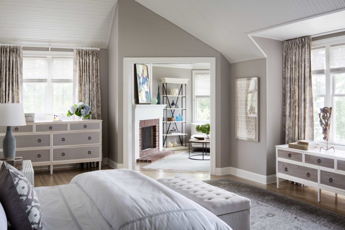 grey master bedroom with fluffy white bedding looking into sun room