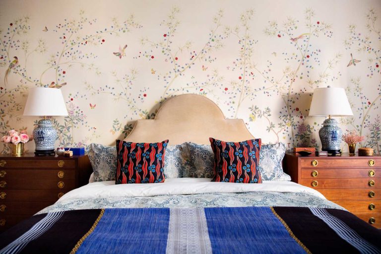 floral wallpaper bedroom with cream headboard and red and blue bed